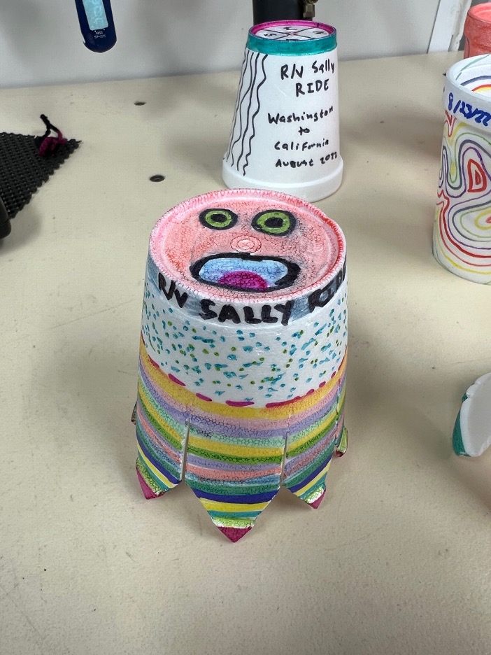 A styrofoam cup decorated with a face, lines, and dots, with the edges cut into "legs" to make it an octopus.
