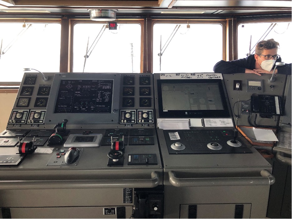 The Captain stands behind a control panel in the Bridge (control room) of the ship.