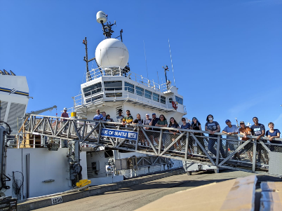 A group of people standing on the gangway of the ship in the Port of Seattle, getting ready to board the R/V Sally Ride. 