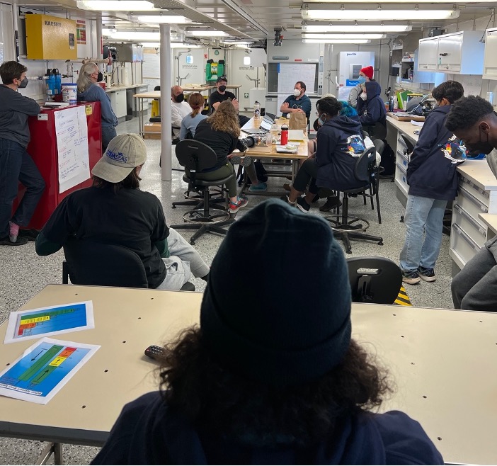 A group of people sitting in a science lab chatting.