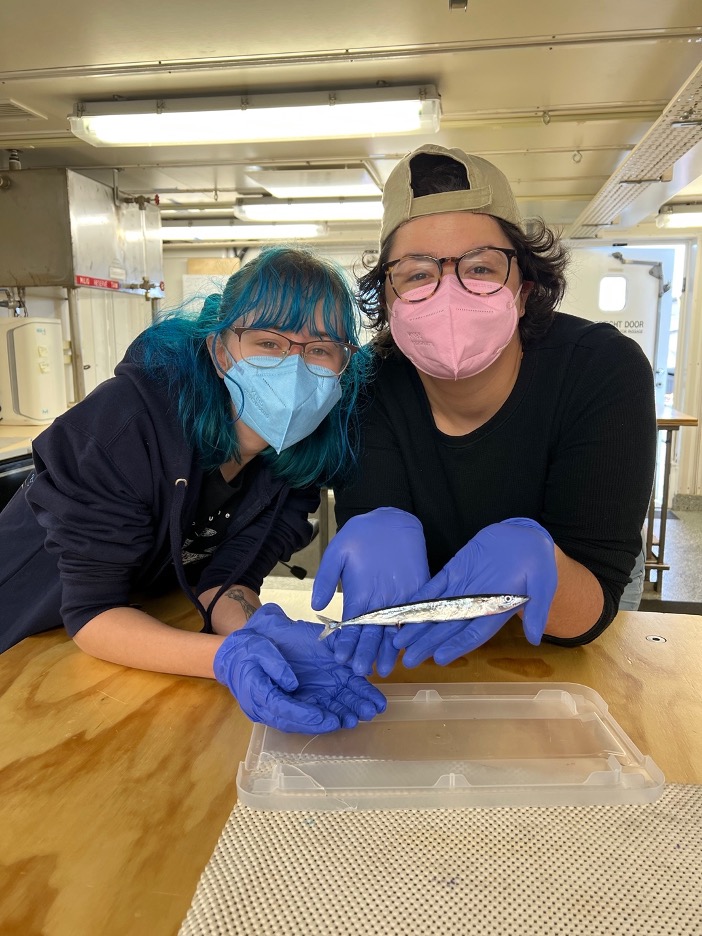 Two students holding a small, long, silver fish.