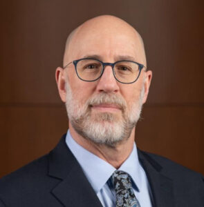 A closeup portrait of Jon Lewis. He is wearing glasses and has a beard.