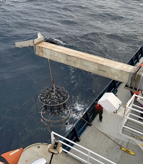 A grey boom lowers a group of instruments into the ocean