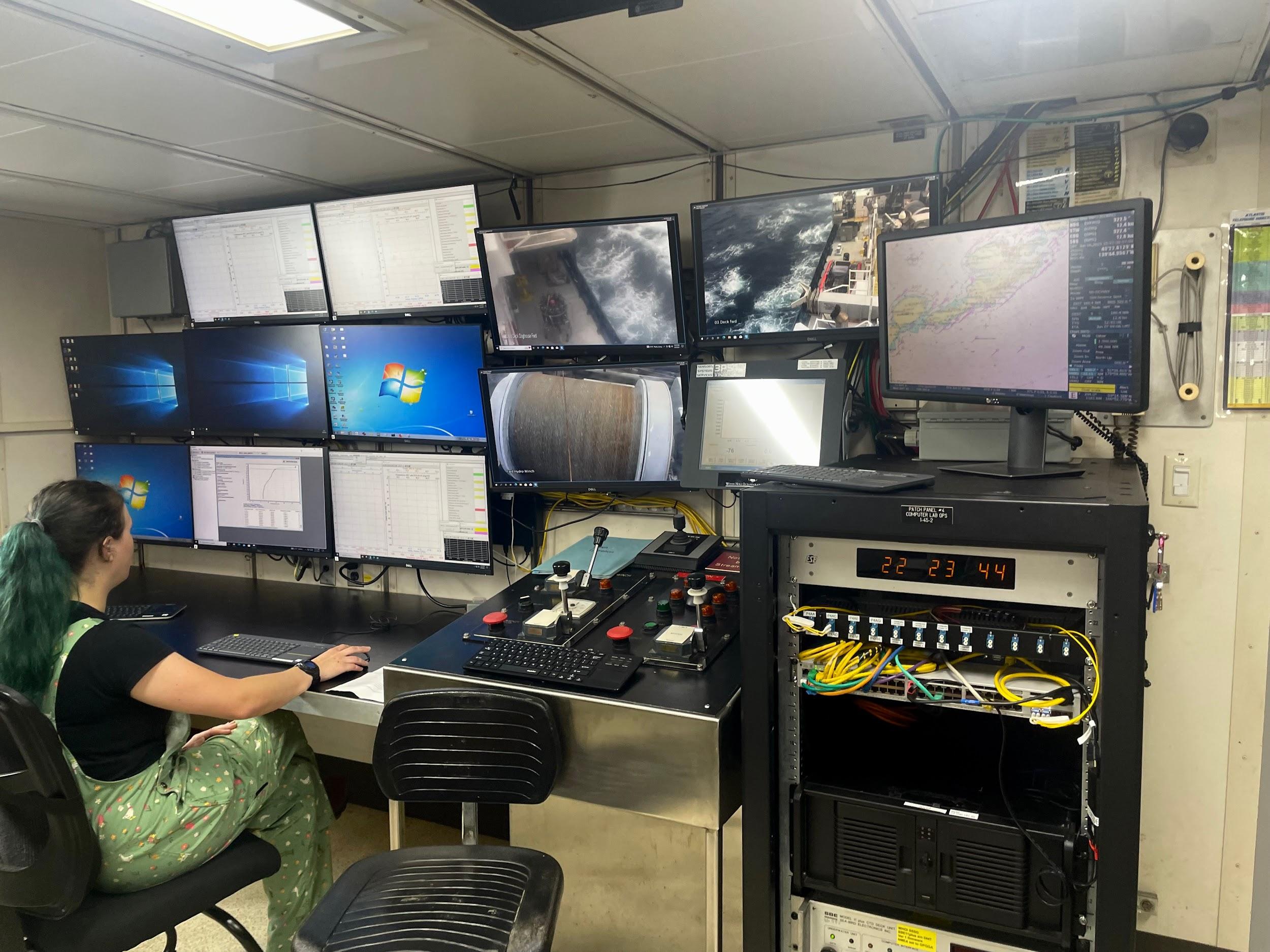 A technician sits in front of a dozen computer monitors covering a wall