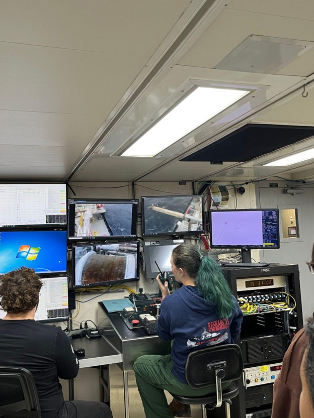 A tech talks on a walkie talkie while watching a video feed on several computer screens