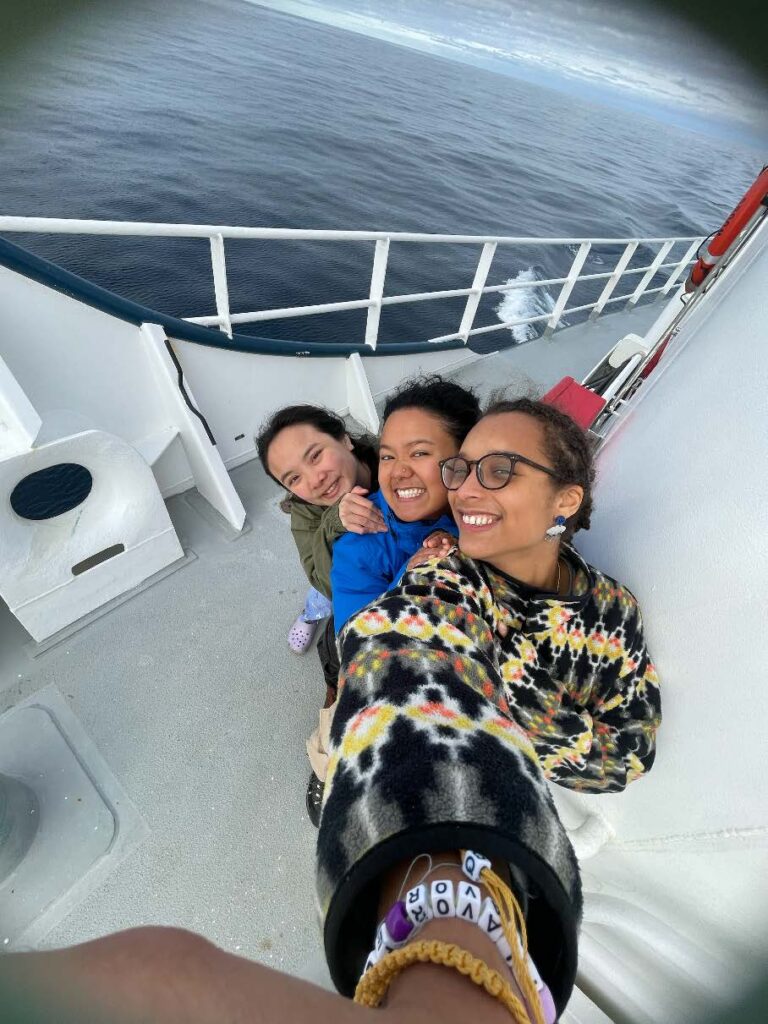 Three scientists smile in a fish-eye view on the deck of a ship