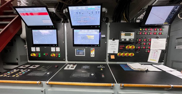 Computer screens with technical data and a black set of panels with buttons and switches