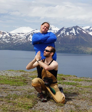 Two students pose comically in front of a beautiful bay and snowy mountains
