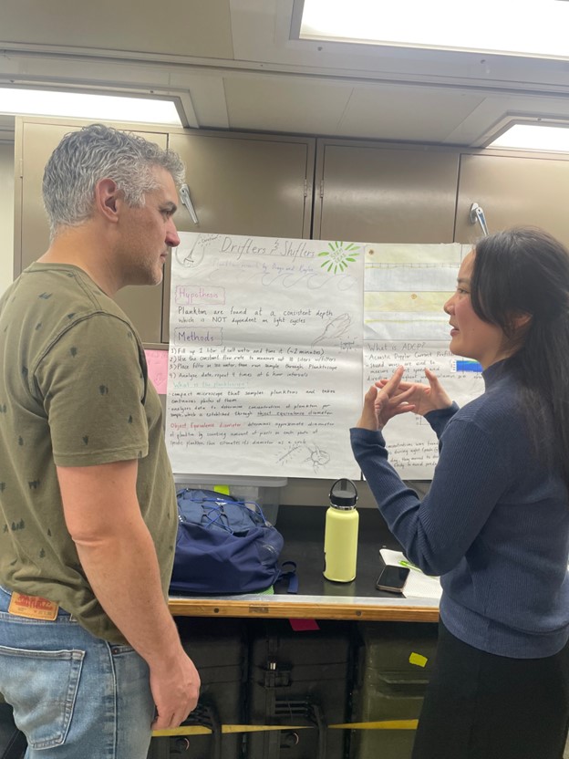 A student gestures to an onlooker in front of a scientific poster