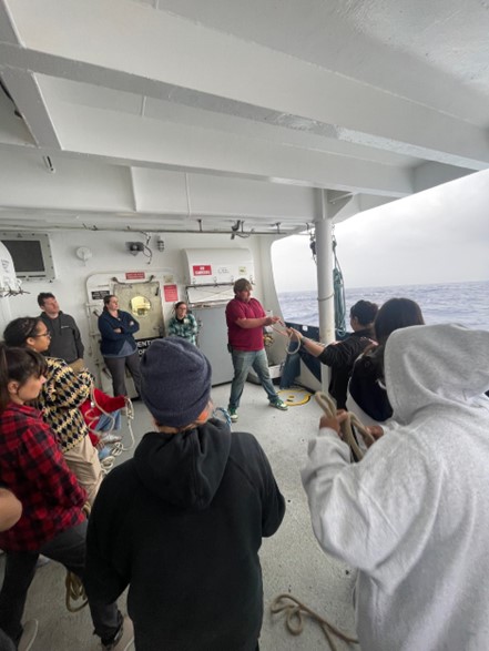 A group of scientists practice tying knots with the ocean in the background