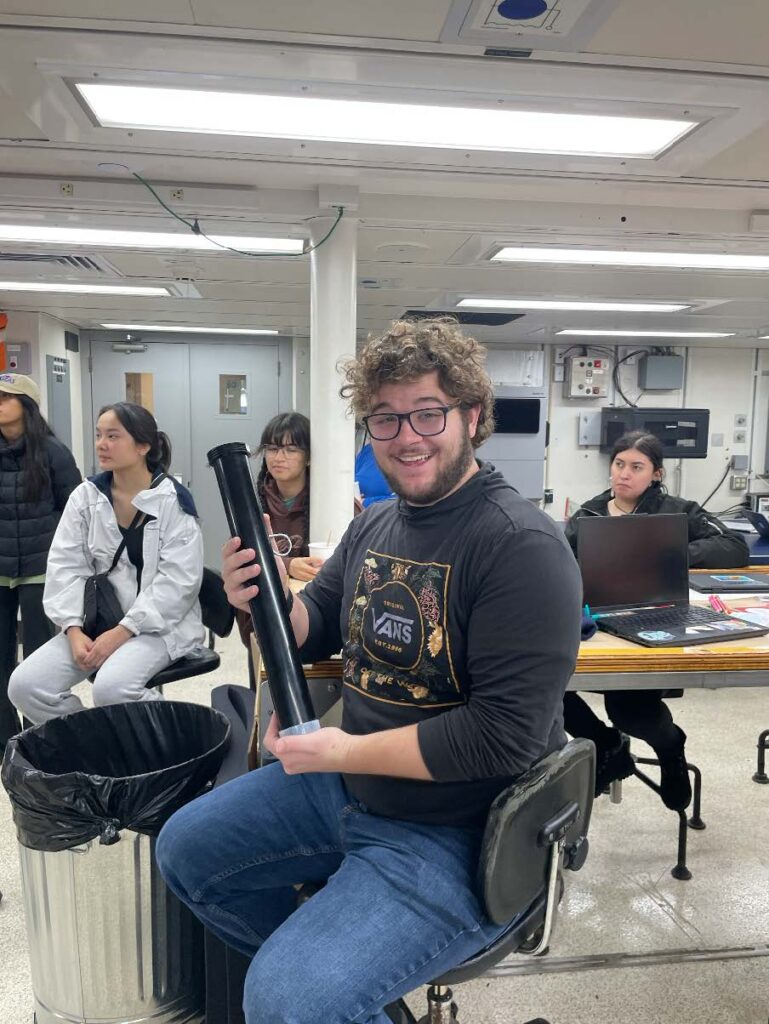 A scientist poses with an instrument that looks like a black pipe
