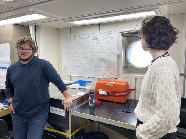 A student casually discusses a scientific poster in front of an onlooker