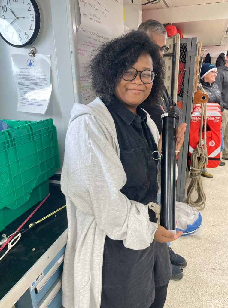 A scientist poses with an instrument that looks like a black pipe