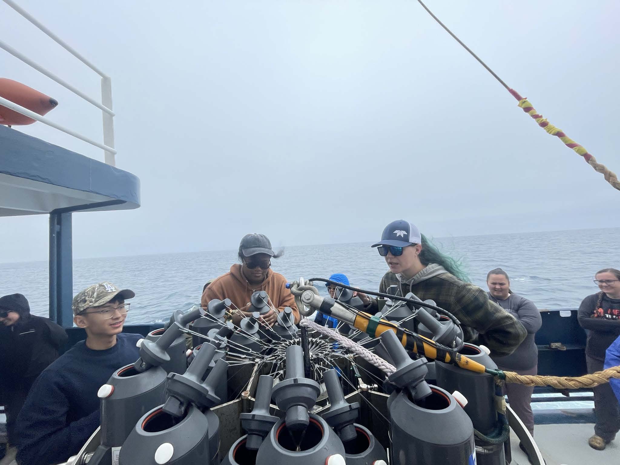 Top view of grey Niskin bottles popped open with three people wearing baseball caps setting them up