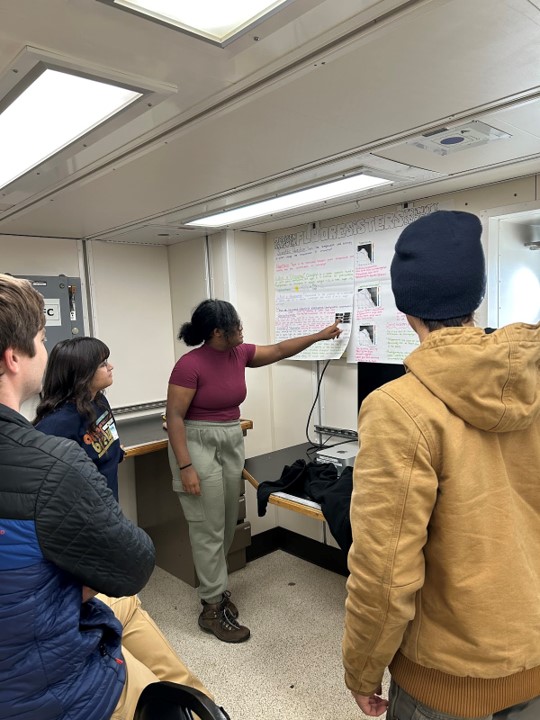 A scientist points to a poster with onlookers listening intently