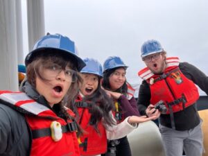 Four scientists with red life vests and blue hard hats make faces at the camera