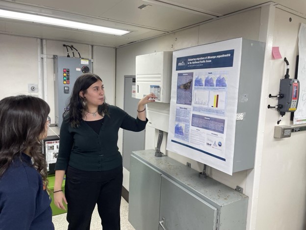 A student points at a scientific poster while another looks on