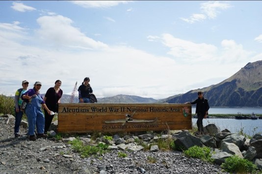 Five hikers stand around a sign reading Aleutian World War II National Historic Area
