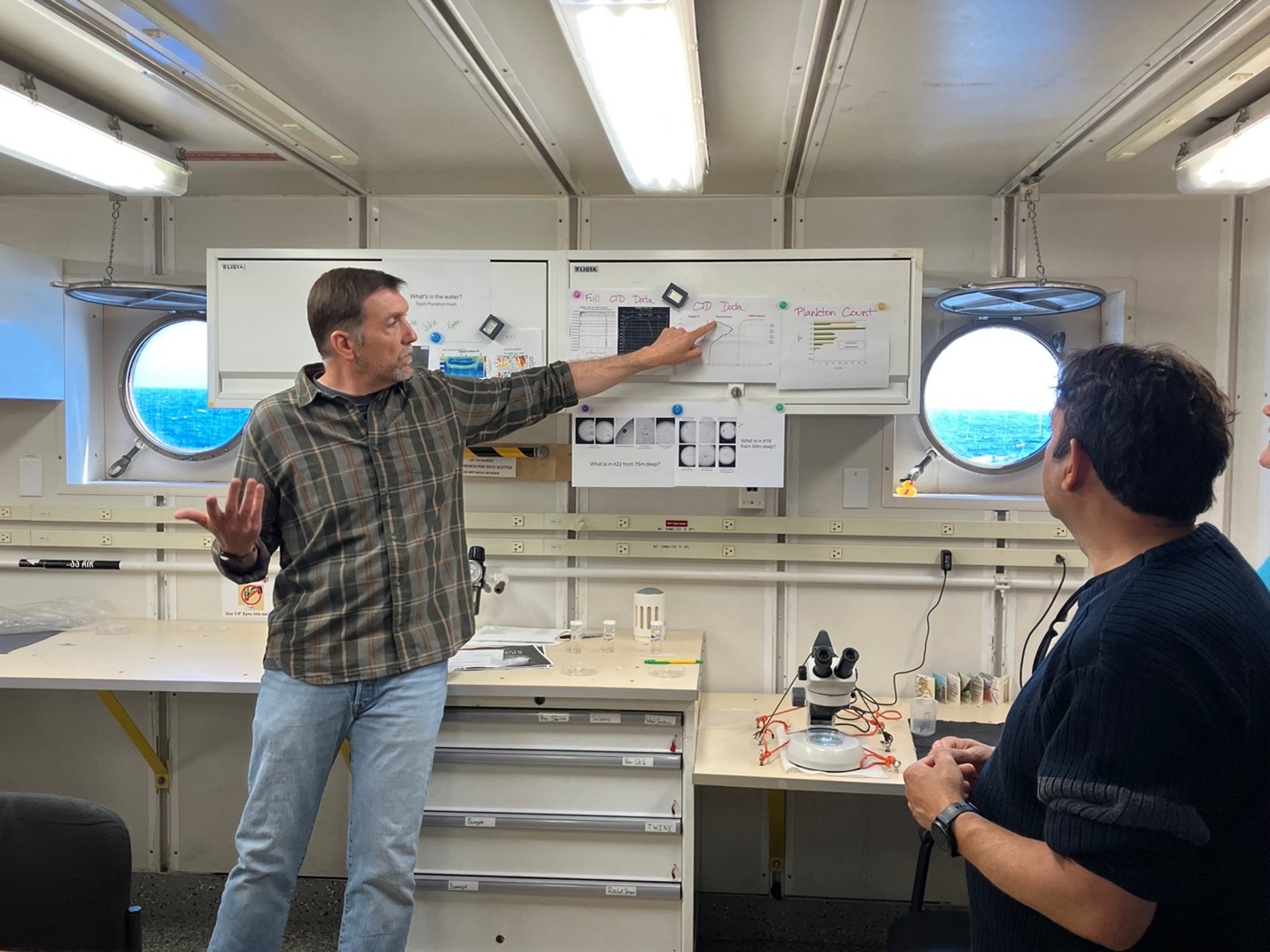 John speaking and pointing at his poster while Anil stands by him